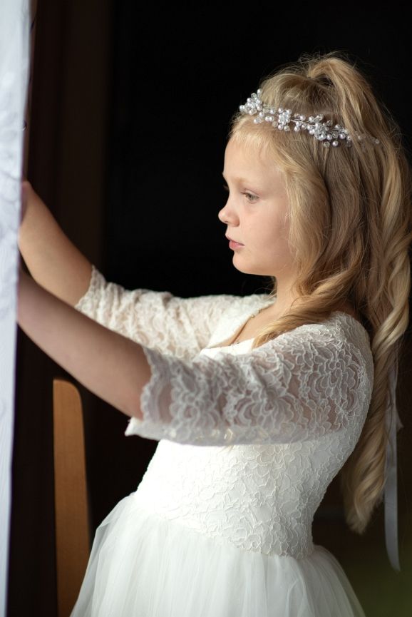 Dziewczynka w białej sukience stoi przy oknie